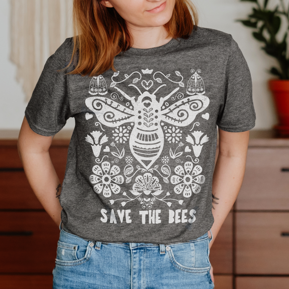 A female model wears a short-sleeved grey t-shirt with a white hand-drawn illustration. The illustration shows a big bumblebee surrounded by stylized flowers and a slogan at the bottom that says 