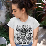 A female model wears a short-sleeved white t-shirt with a black hand-drawn illustration. The illustration shows a big bumblebee surrounded by stylized flowers and a slogan at the bottom that says "save the bees".